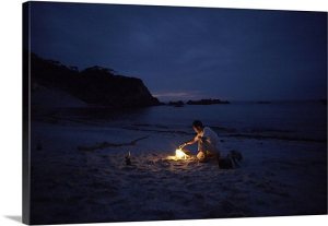 man-sitting-by-campfire-on-beach-at-night-200573358-001